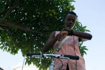 Mulher com bicicleta usando smartwatch na rua da cidade em um dia ensolarado — Fotografia de Stock