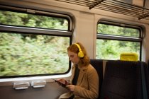 Молодая женщина листинг на музыку во время использования планшета в поезде — стоковое фото