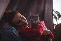 Primer plano de la mujer sonriente abrazando a su gato mascota en casa - foto de stock