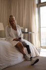 Reife Frau mit Beinprothese mit Handy im heimischen Schlafzimmer. — Stockfoto