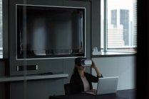 Деловая женщина в наушниках виртуальной реальности во время работы над ноутбуком в офисе — стоковое фото