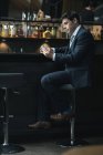 Uomo d'affari che usa il cellulare mentre beve whisky al bancone dell'hotel — Foto stock