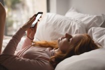 Mujer usando teléfono móvil en el dormitorio en casa - foto de stock