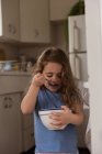 Menina comendo de uma tigela na cozinha — Fotografia de Stock