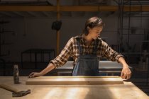 Jovem mulher artesã medindo peça de madeira na oficina . — Fotografia de Stock