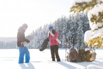 Casal de pé junto com mochilas e equipamento de esqui em paisagem nevada . — Fotografia de Stock