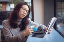 Mulher bonita ler revista enquanto toma café na cafetaria — Fotografia de Stock