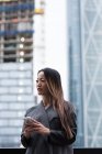 Donna d'affari guardando altrove mentre usando il suo telefono cellulare in piedi contro l'edificio della città — Foto stock