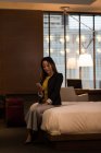 Деловая женщина, сидящая на кровати с помощью мобильного телефона в отеле — стоковое фото