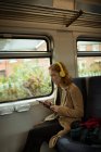 Молодая женщина листинг на музыку во время использования планшета в поезде — стоковое фото