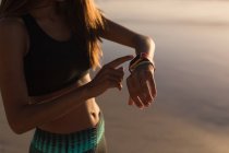 Donna in forma utilizzando smartwatch sulla spiaggia al tramonto . — Foto stock