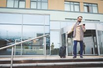 Uomo d'affari che esce dall'hotel mentre usa il cellulare in una giornata di sole — Foto stock