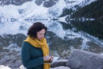 Женщина-туристка с помощью цифрового планшета на берегу озера зимой — стоковое фото