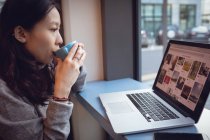 Mulher bonita usando laptop enquanto toma café na cafetaria — Fotografia de Stock