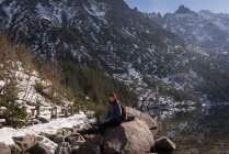 Туристка зимой сидит на скале у озера — стоковое фото