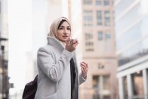 Mujer en hijab hablando por teléfono móvil en la calle de la ciudad - foto de stock