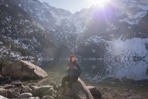 Caminhante feminina sentada na rocha à beira do lago durante o inverno — Fotografia de Stock