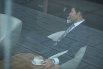 Empresario hablando por teléfono móvil mientras toma café en la oficina - foto de stock