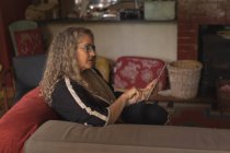 Зрелая женщина с цифровым планшетом на диване в гостиной — стоковое фото