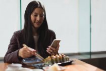 Junge Frau benutzt Handy beim Essen im Restaurant — Stockfoto