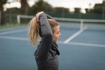 Молодая женщина, стоящая с руками на волосах на теннисном корте — стоковое фото