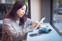 Красива жінка використовує цифровий планшет, маючи каву в кафетерії — стокове фото