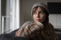 Thoughtful woman in woolly hat in living room at home. — Stock Photo