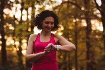 Femme utilisant montre intelligente en forêt un jour de saison — Photo de stock