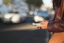 Sección media de la mujer usando el teléfono móvil en la calle de la ciudad - foto de stock