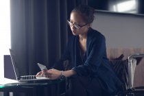 Женщина за столом в офисе с помощью мобильного телефона и ноутбука — стоковое фото
