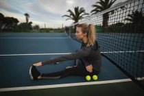 Mujer joven realizando ejercicio de estiramiento en la cancha de tenis - foto de stock