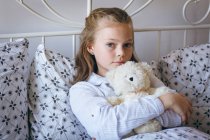 Mädchen hält Teddybär auf Bett im Schlafzimmer — Stockfoto