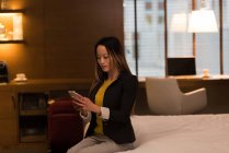 Деловая женщина, сидящая на кровати с помощью мобильного телефона в отеле — стоковое фото