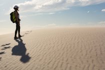 Caminhante feminina com mochila em pé na areia em um sol — Fotografia de Stock