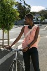 Продумана жінка стоїть з велосипедом на міській вулиці — стокове фото