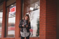 Bella ragazza rivedere l'immagine sulla fotocamera digitale al di fuori del centro commerciale — Foto stock