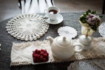 Cup of tea with raspberry bowl and tea pot on table at home — Stock Photo