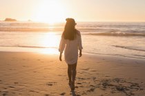 Woman walking in sandy beach at sunset. — Stock Photo