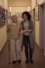 Доглядач допомагає старшому чоловікові під час прогулянки в коридорі в будинку престарілих — стокове фото