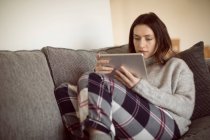 Donna che utilizza tablet digitale sul divano in soggiorno a casa . — Foto stock