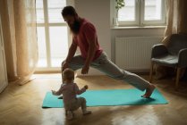 Bebê imitando seu pai enquanto se exercita em casa — Fotografia de Stock