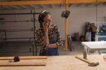 Joven artesana hablando por teléfono móvil en taller . - foto de stock
