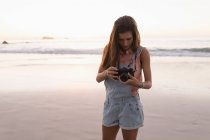 Mujer sosteniendo la cámara en la playa al atardecer . - foto de stock