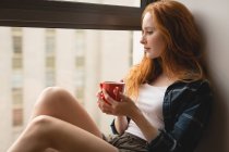 Задумчивая женщина пьет кофе дома — стоковое фото