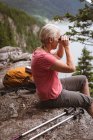 Side view of mature woman sitting on rock looking through binoculars — Stock Photo