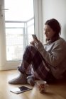 Jeune femme utilisant un téléphone portable tout en étant assis sur le sol à la maison
. — Photo de stock