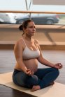 Femme enceinte effectuant du yoga dans le salon — Photo de stock