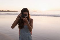 Donna che scatta foto con macchina fotografica in spiaggia al tramonto . — Foto stock