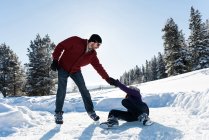 Hombre ayudando a la mujer a levantarse mientras patina en el paisaje nevado . - foto de stock