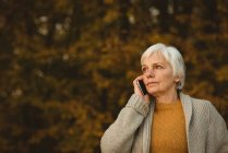 Старшая женщина использует смартфон в парке на рассвете — стоковое фото